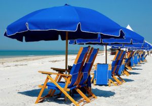 a row of blue lounge chairs and umbrellas at the beach