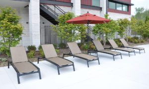 a row of brown lounge chairs and a red standing umbrella