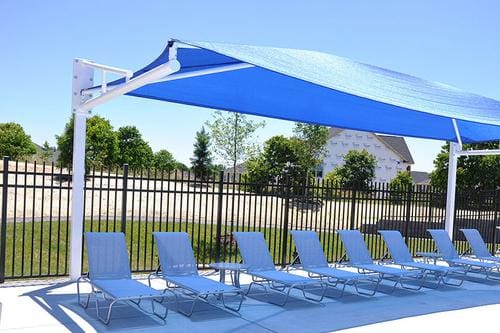 A blue umbrella over some white lounge chairs.