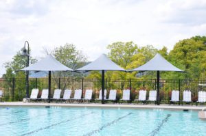 a row of lounge chairs with three standing umbrellas by the pool